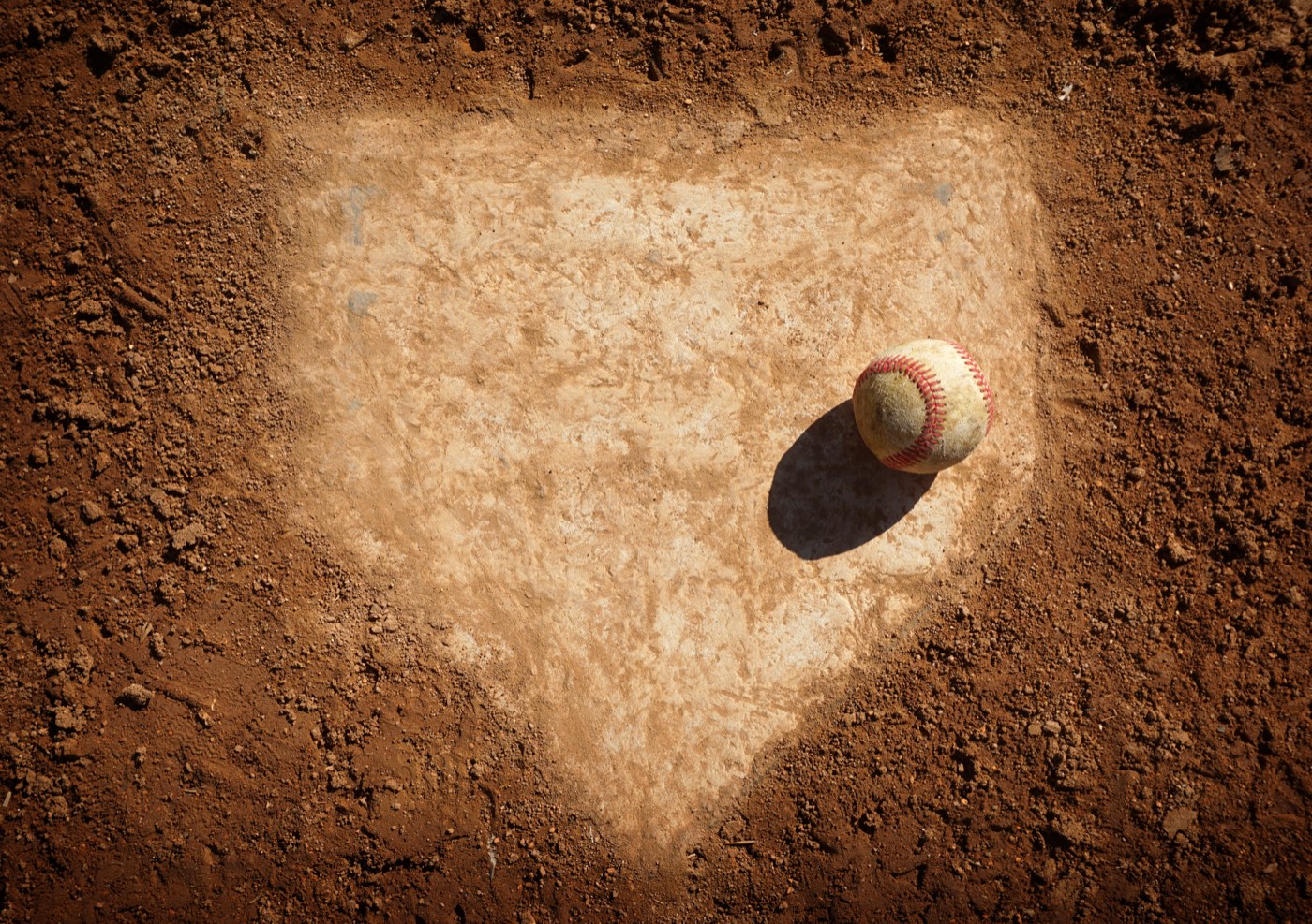 A baseball resting on home plate on a dirt infield