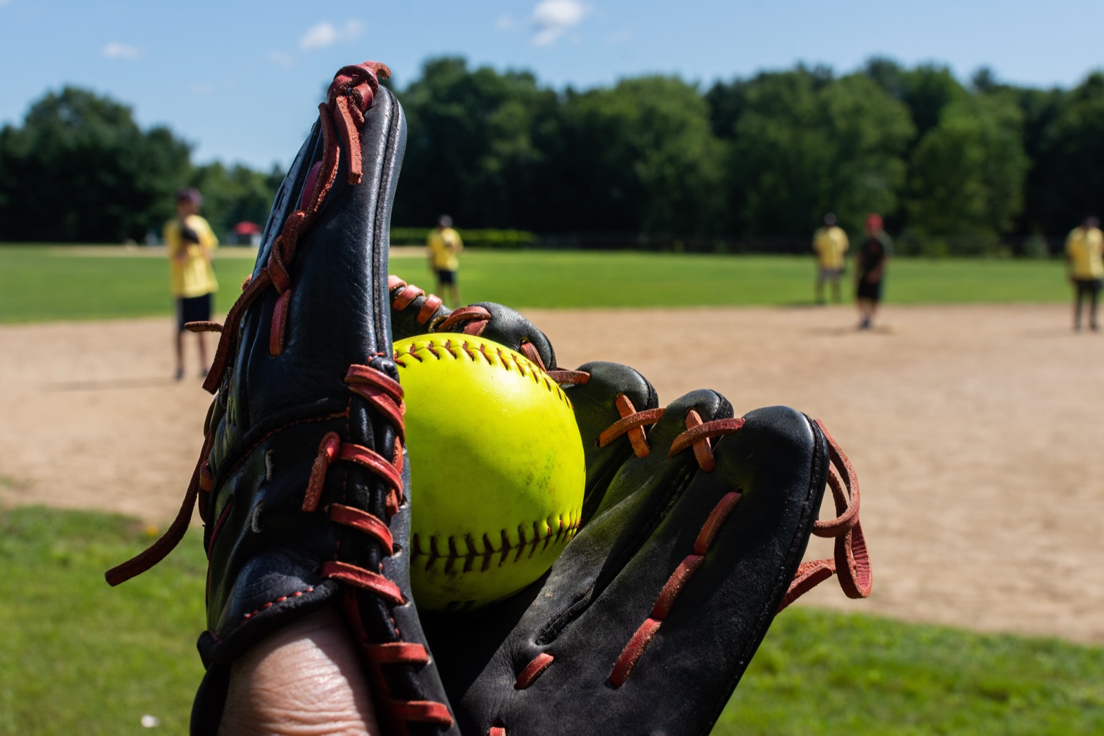 A yellow softball caught in a leather glove on a sunny field